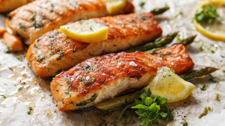 Baked salmon filets with aromatic herbs and lemon on baking paper close up view