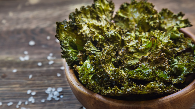 kale chips in bowl on wooden table with salt 