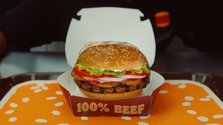A Burger King Whopper, partially wrapped in paper and in a burger box, on a dine-in tray