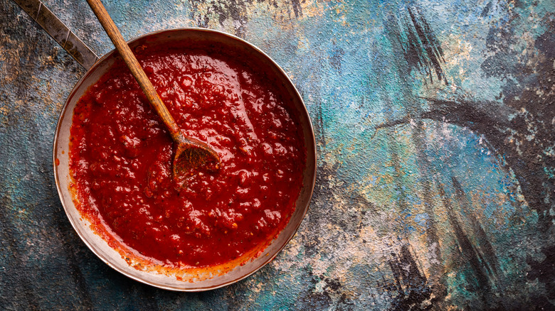 Pot of red tomato sauce with wooden spoon on rustic surface