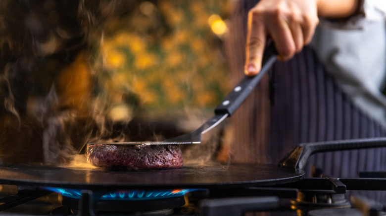 Person smooshing patty on grill