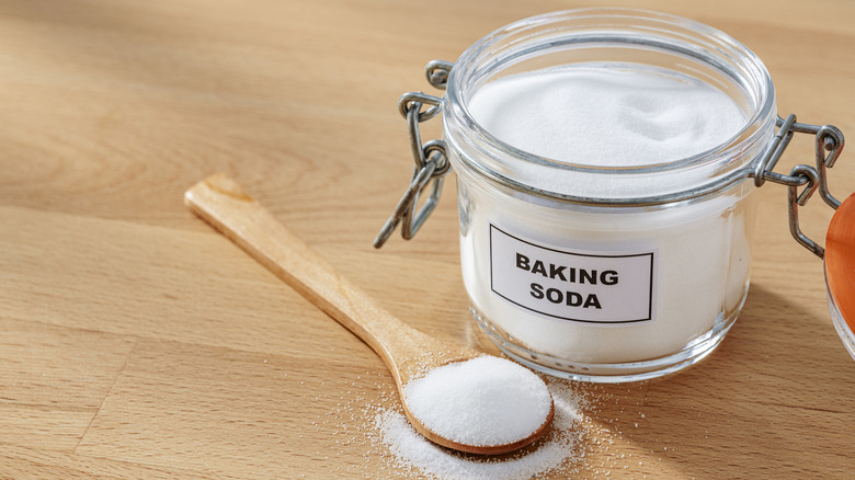 A glass jar of baking soda next to baking soda on a wooden spoon