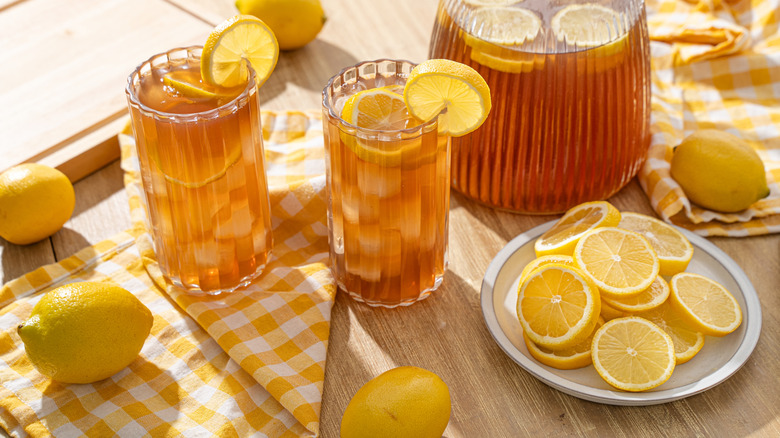 Two glasses of Arnold Palmer next to a pitcher and a lot of lemons