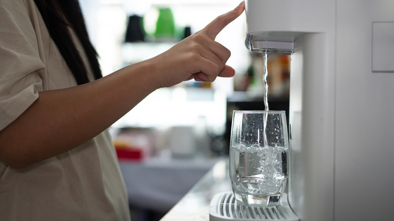 A person uses a water filtration system at home to pour a glass of water