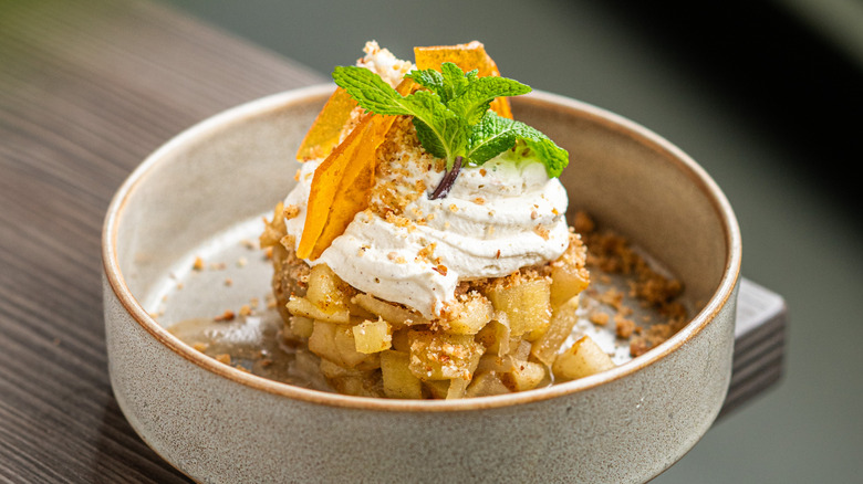 An apple crisp dessert with cream, candied citrus, and mint leaves