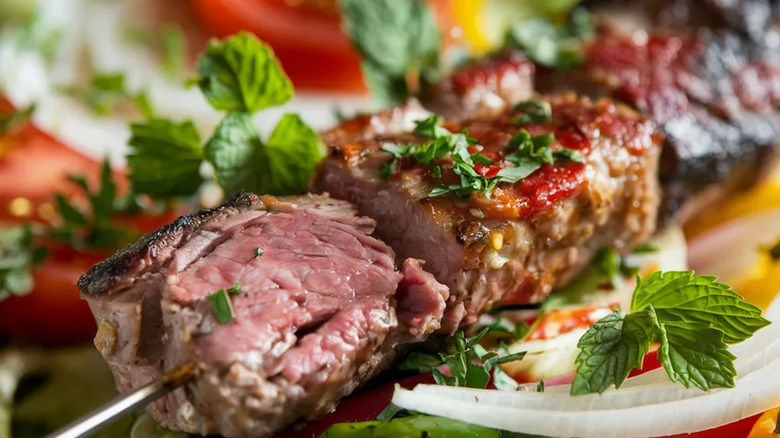 Close up of a skewer of steak kebab with an herb garnish.