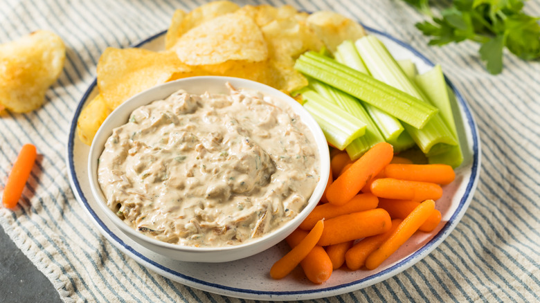 Caramelized onion dip in a bowl with potato chips, and celery and carrot batons