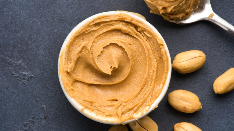 A bowl of creamy peanut butter with peanuts scattered about