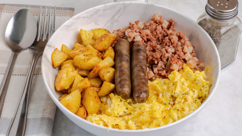 White marble bowl of potatoes, hash, sausage, and scrambled eggs