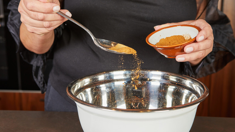 Person making mixed spice in metal bowl