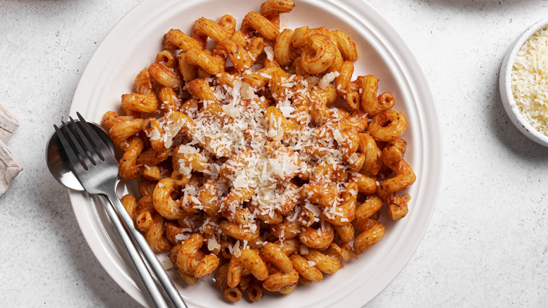 A plate of tubular tomato pasta, with cheese on top