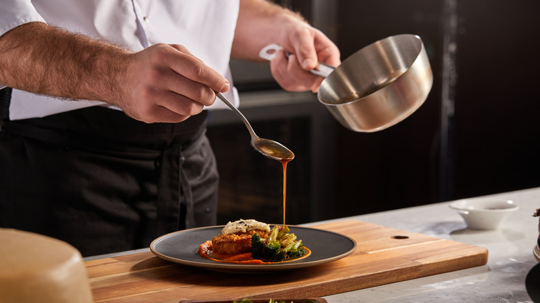 Chef pouring sauce over food