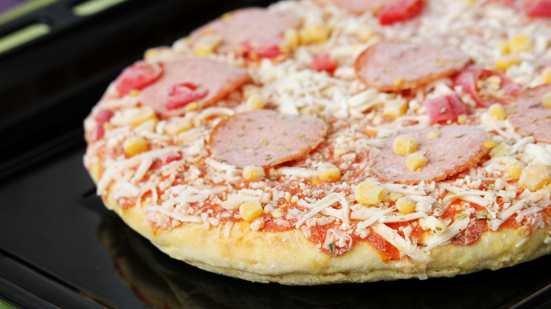 A frozen pizza with pepperoni and corn on a black tray