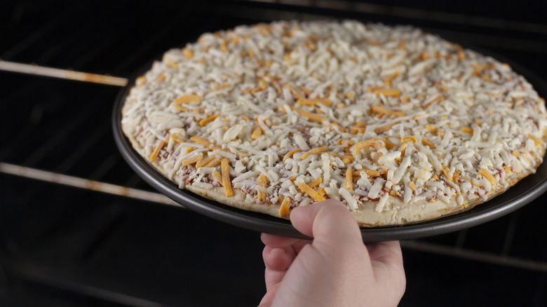 A person putting a frozen pizza inside an oven