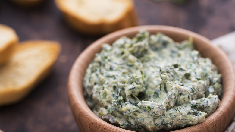 brown bowl of spinach dip with toasted bread in background