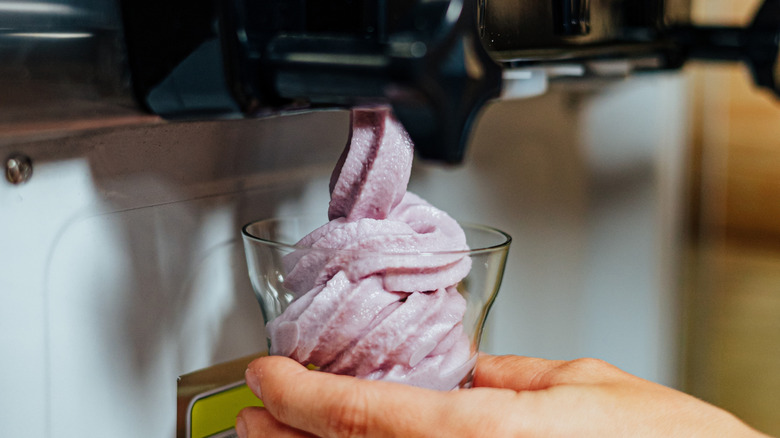 A hand holding soft serve or frozen yogurt being dispensed by a soft serve machine