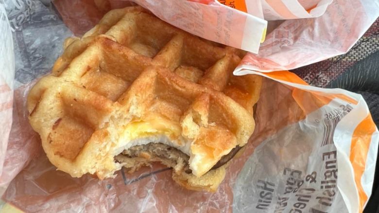 A close-up of a waffle breakfast sandwich from Kwik Trip in branded paper