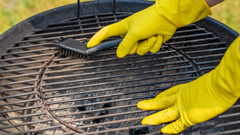 Person with yellow gloves cleaning a round charcoal grill