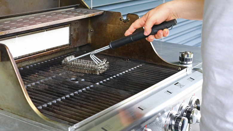 Person using wire scrubber to clean gas grill
