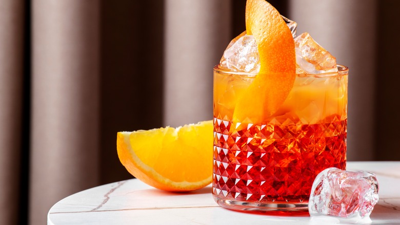 A glass containing a Negroni Sbagliato with an orange peel in it and an orange slice beside it