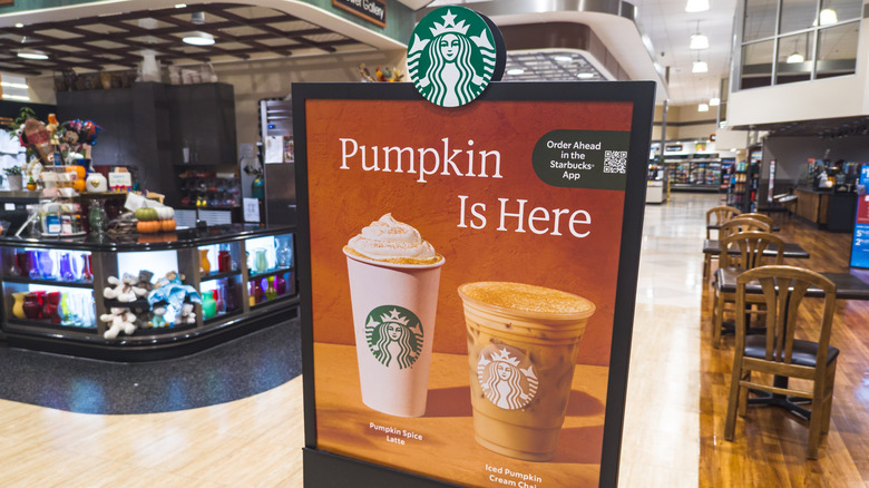 A Starbucks sign advertising that "Pumpkin Is Here," with images of a Pumpkin Spice Latte and Iced Pumpkin Cream Chai