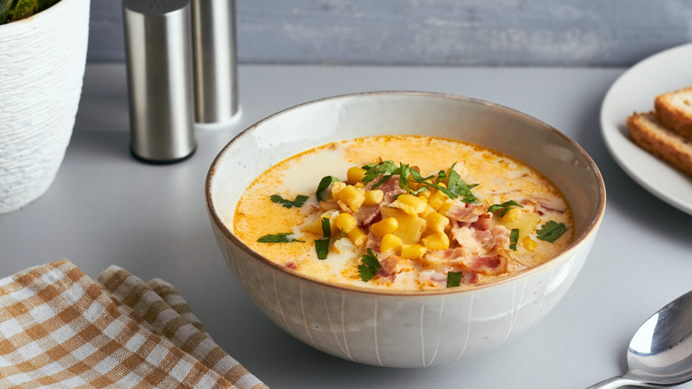 A bowl of corn chowder with green onions, potatoes, and bacon