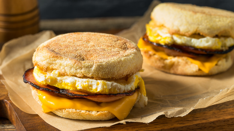 Two breakfast sandwiches with egg, bacon, and cheese on a wrapper on a table