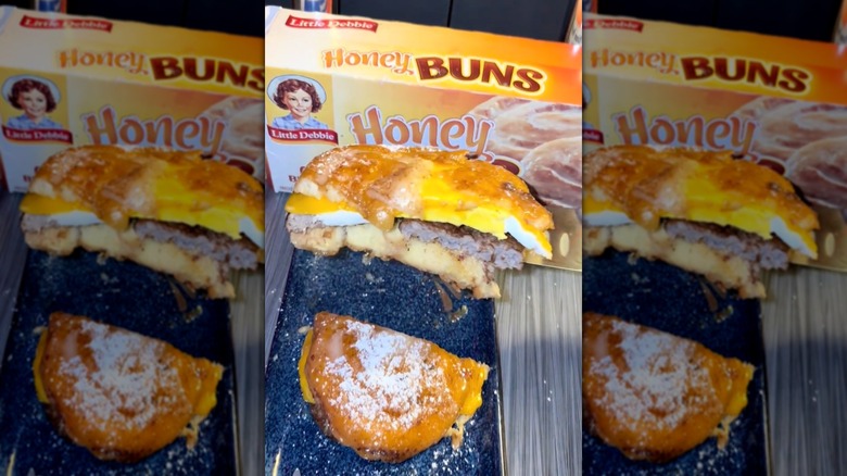 A hand showing off the cross section of a Honey Bun breakfast sandwich in front of a Little Debbie Honey Buns box