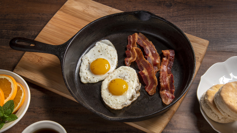 Fried eggs and bacon in skillet with biscuits and coffee