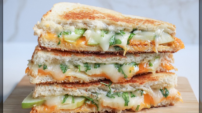 Three pieces of an apple cheddar grilled cheese stacked on a wood board