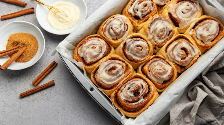A deep baking sheet covered in parchment paper with glazed cinnamon rolls on it
