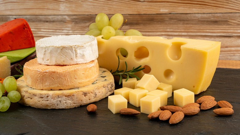 Several varieties of cheese stacked on a table with grapes and nuts