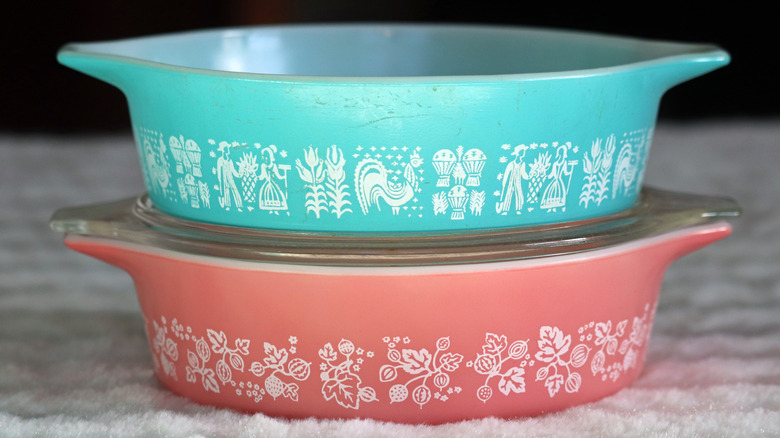 A stack of two vintage Pyrex casserole dishes, one in pink and one in blue, with one clear glass lid