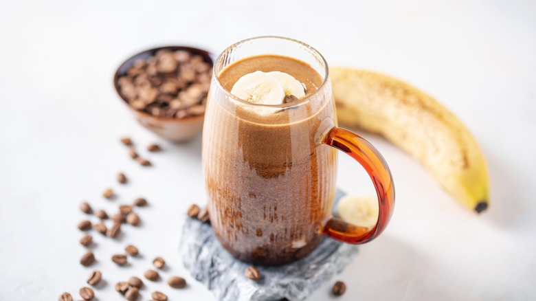 mug of banana coffee with a banana and coffee beans in the background