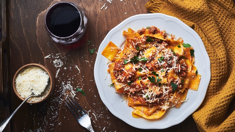 pasta with bolognese sauce in bowl on counter with yellow dish cloth, wine, cheese