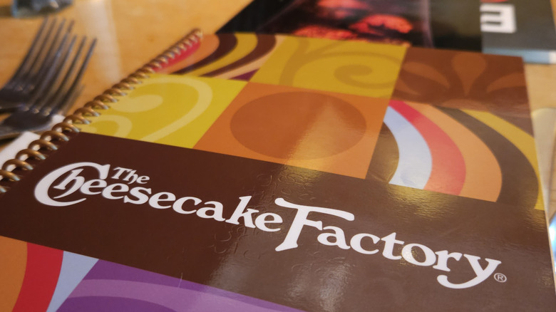 Cheesecake factory menu on a table next to two forks