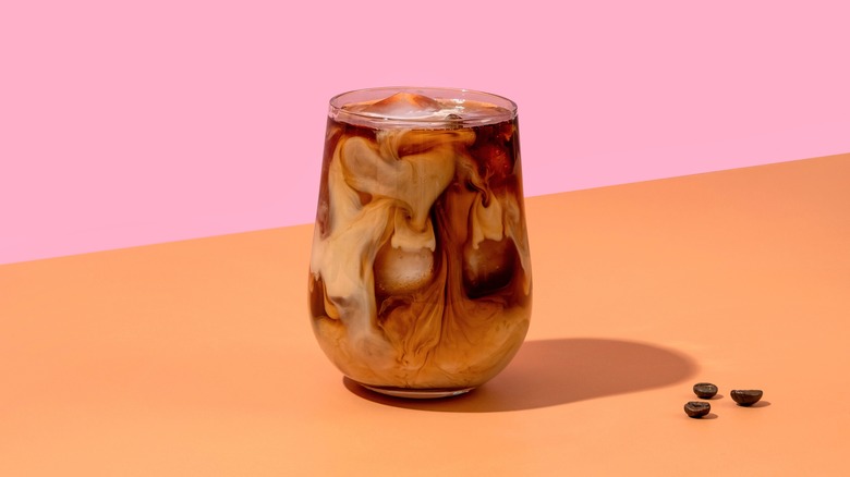 Glass of milky iced coffee on orange and pink background