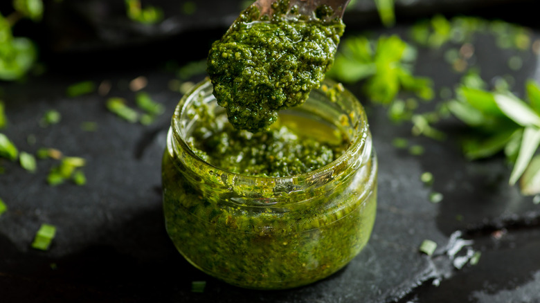 Jar of green pesto among herbs