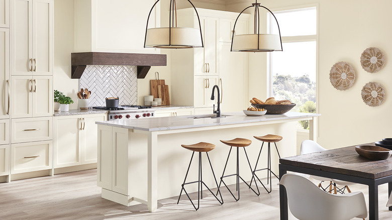 warm white modern kitchen with linen pendant lights, wooden and iron barstools, and hanging wall baskets.