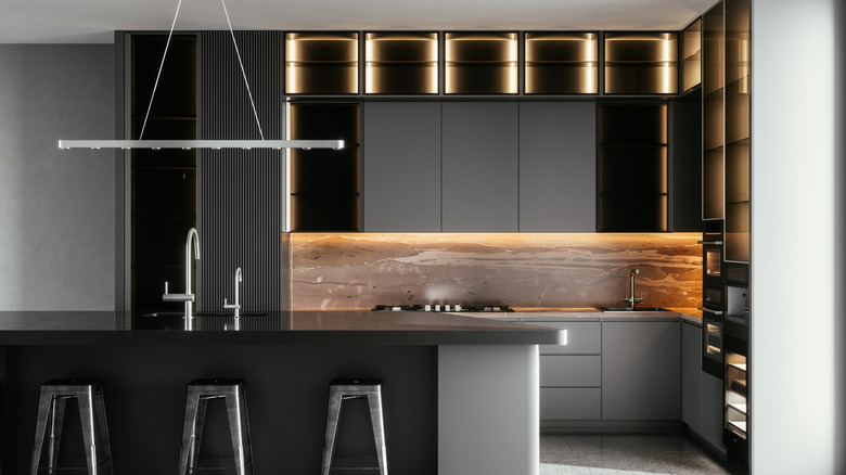 dramatic dark grey kitchen with a modern lighting and cabinets and metal barstools.