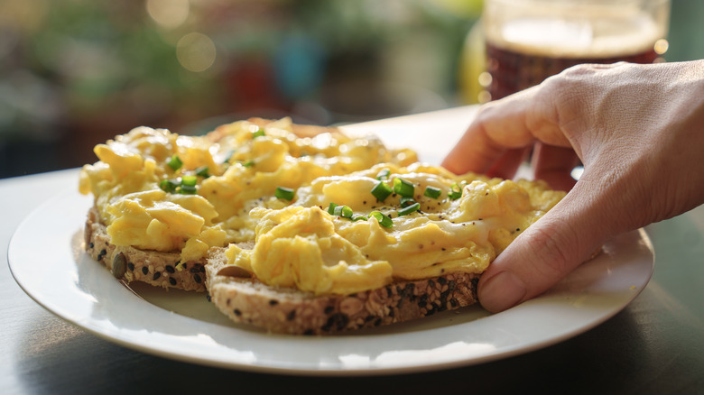 hand grabbing Scrambled eggs on toast on plate