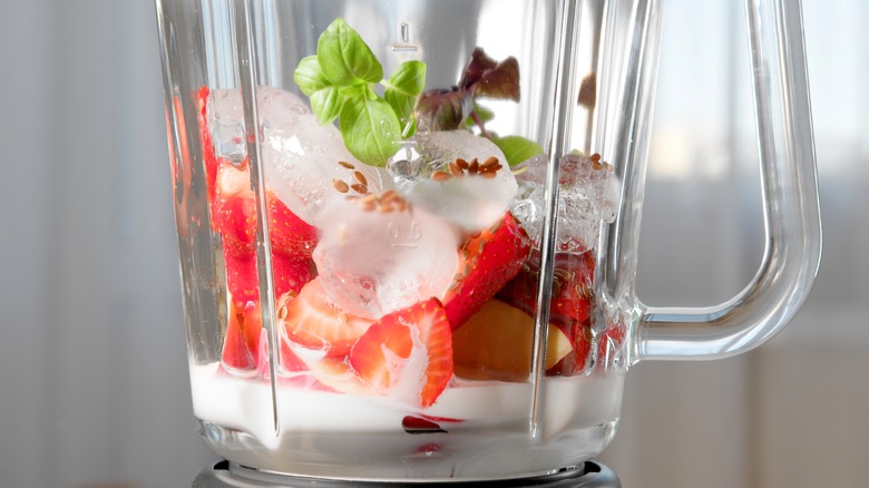 Close up of a glass blender with ice, milk and strawberries