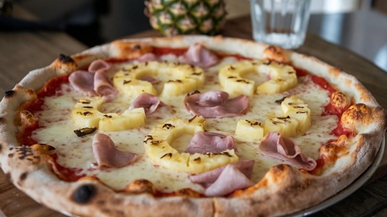 Whole Hawaiian pizza topped with ham and pineapple on table.