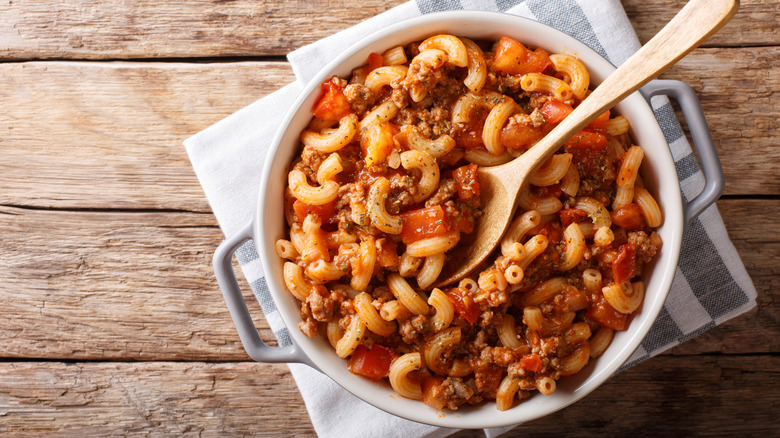 Overhead shot of american goulash in a white pot, styled on a rustic table.