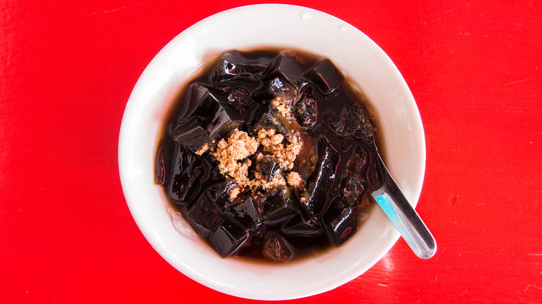 grass jelly in a bowl with sugar and red background