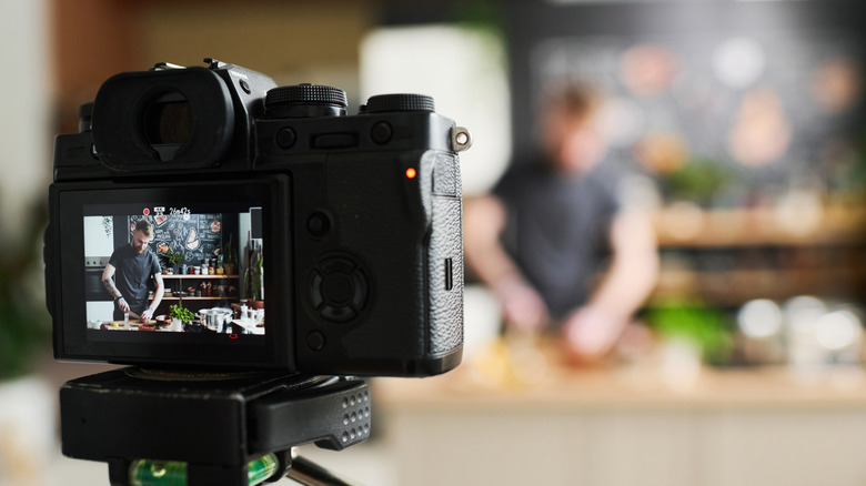 A camera set up to record a man chopping ingredients in a kitchen