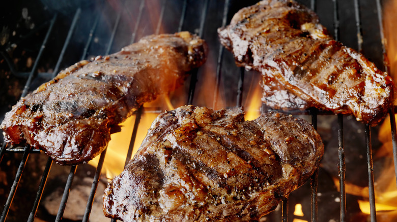 steaks roasting over fiery grill