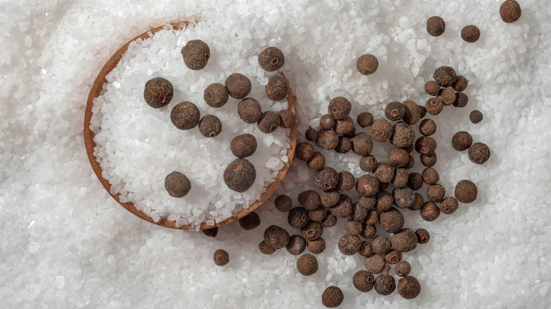 Salt in a wooden bowl and on a table with black peppercorns on top
