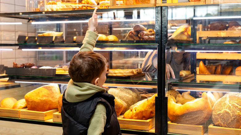 A boy pointing for a baked treat inside a bakery case