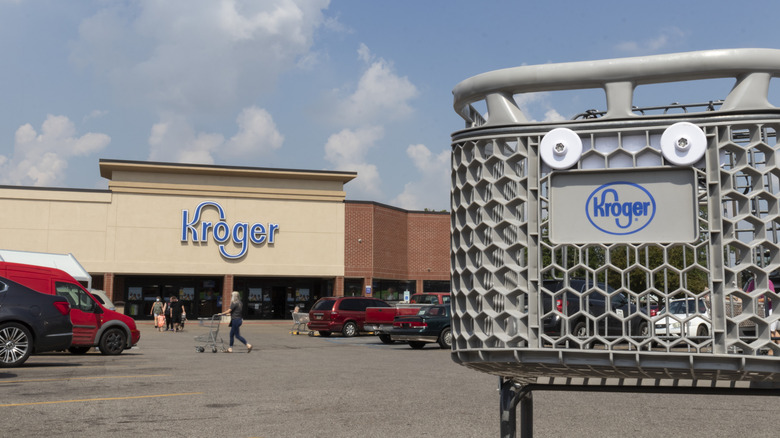 A Kroger shopping cart in the foreground, with a Kroger store exterior in the background